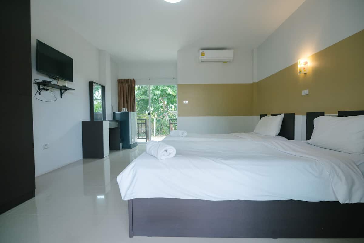 A hotel room with two beds, a flat-screen TV mounted on the wall, an air conditioning unit, and a view of greenery through the window.