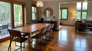 Un salón amplio con una gran mesa de comedor de madera, asientos cómodos, una chimenea y ventanas grandes que ofrecen vistas al exterior.