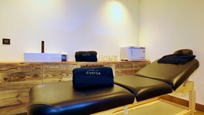 A massage therapy room with a wooden reception desk, a massage table, and a towel with "Chalet Coston" branding.