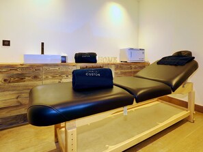 A massage therapy room with a wooden reception desk, a massage table, and a towel with "Chalet Coston" branding. - Luxury Chalet 10 pers, SPA, pool, WiFi, Courchevel 1550 (Courchevel 1550)