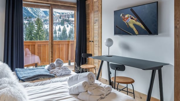 Ett hotellrum med en säng, ett skrivbord, en stol, en TV och utsikt över bergen.
