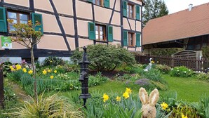 Un jardin agrémenté de diverses espèces de fleurs, une statue de lapin décorative et un bâtiment à la façade traditionnelle en colombages.