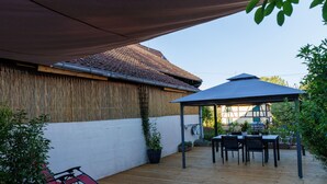 Une terrasse extérieure couverte, avec une table et des chaises, un fauteuil suspendu et une plante en pot.