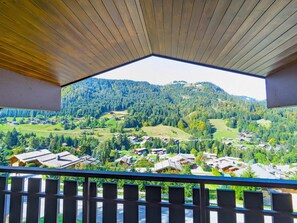 Vista da un balcone con soffitto in legno, su un villaggio immerso in una valle circondata da colline boschive.
