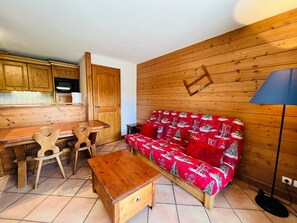 Una habitación acogedora con paredes de madera, un sofá rojo con diseño invernal, una mesa de madera y un banco.