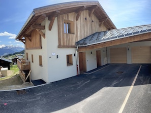 A building with a sloped roof, wooden exterior, and a parking area with a clear view of mountains in the background. - 4-room apartment Les Saisies for 6, garage included (Les Saisies)