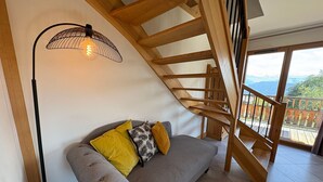 A modern interior with a grey sofa, wooden staircase, and a view through a large window.