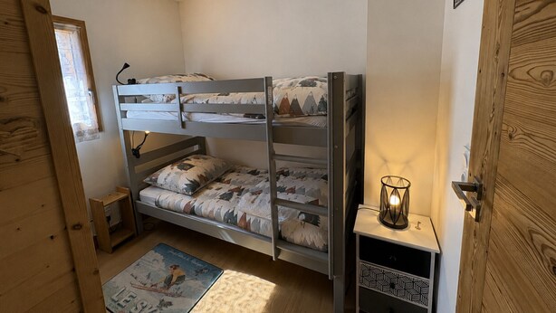 A bunk bed with a patterned bedspread, a bedside table with a lamp, and a small shelf.