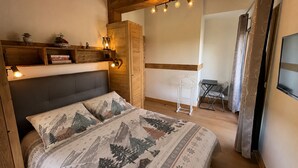 A bedroom with a bed, bedside tables, a wooden headboard, a hanging light fixture, and a view into an adjacent room.