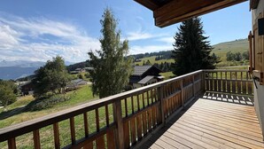 A wooden deck with a railing overlooking a rural landscape with houses and trees.