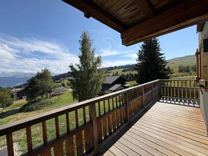 A wooden deck with a railing overlooking a rural landscape with houses and trees.