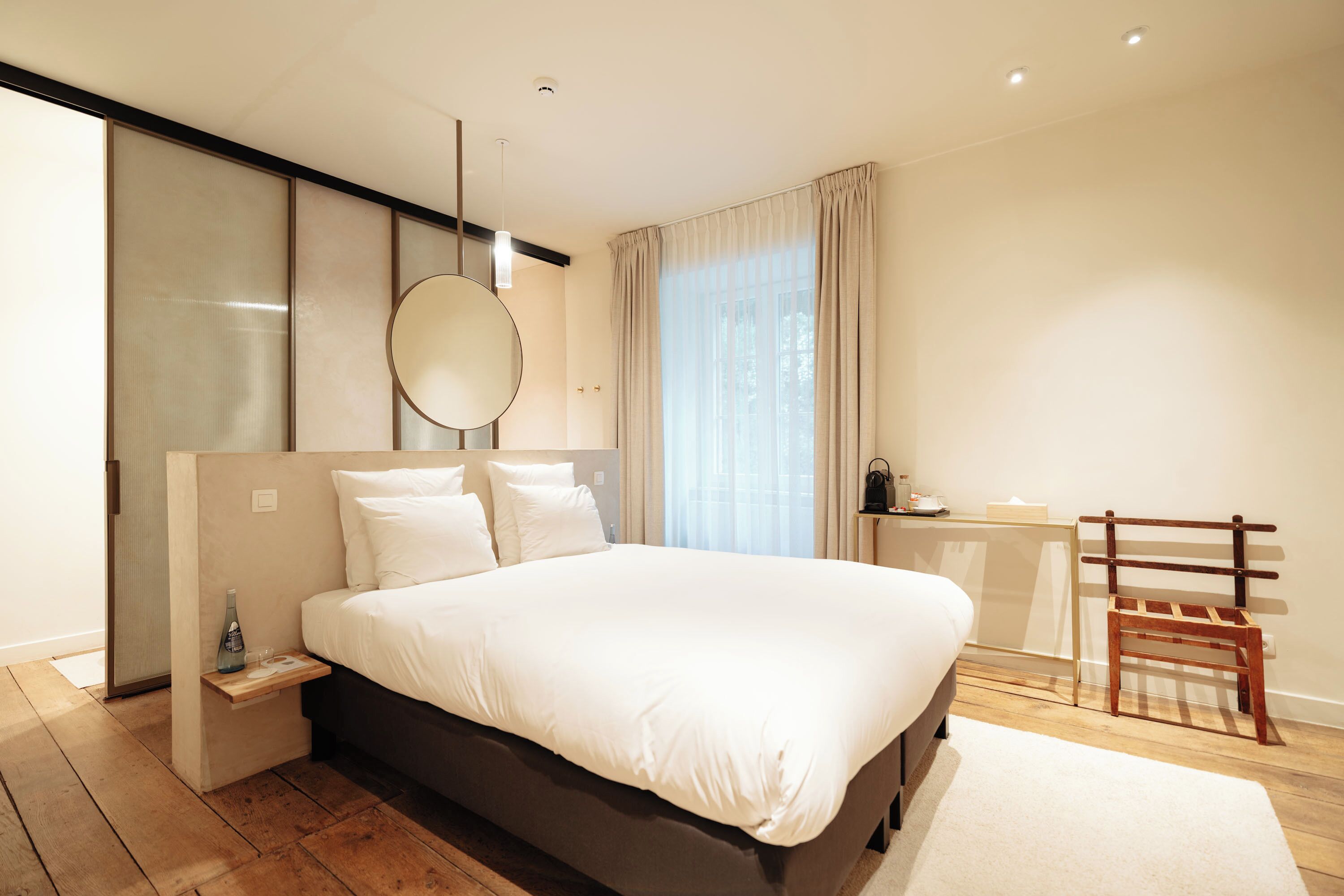 Un dormitorio moderno con una cama grande, una mesita de noche, un espejo y una silla de madera.