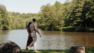 A couple walking by a lake with trees in the background.