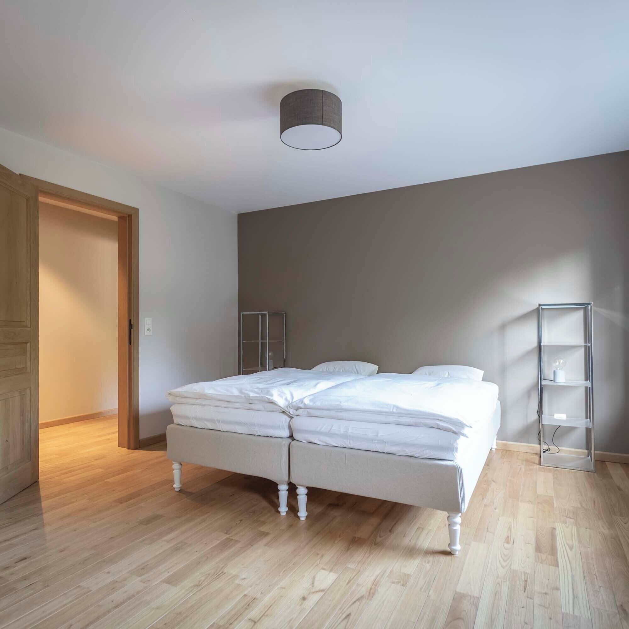 A bedroom with a bed, a wardrobe, a shelf unit, and a ceiling light fixture.