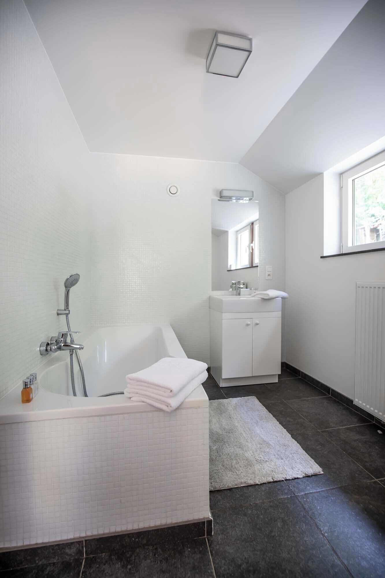 Een moderne badkamer met een vrijstaand bad, een wastafel met spiegel en een raam voor natuurlijk licht.