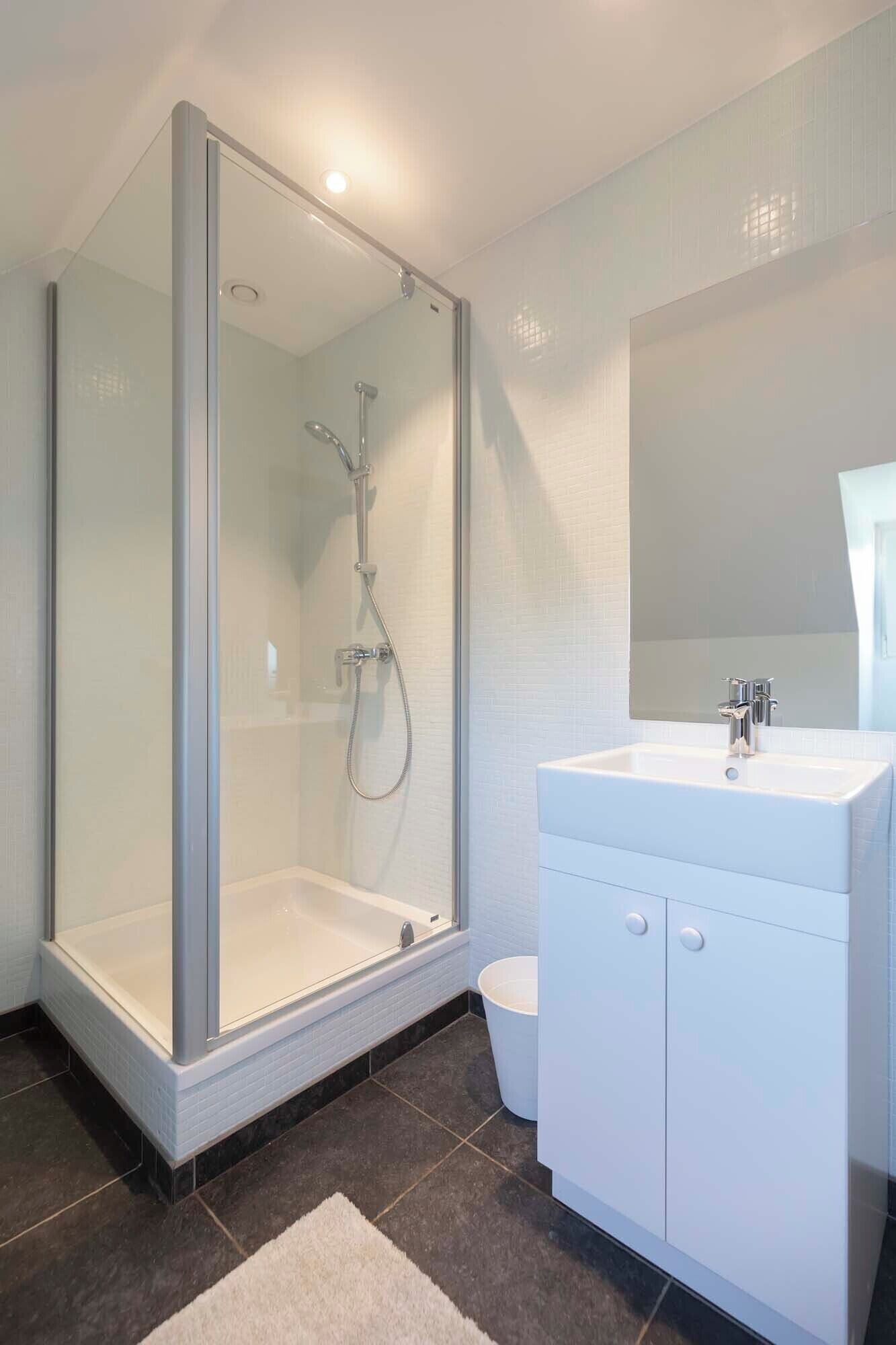 Un baño moderno con ducha vidriada, un lavamanos blanco y un espejo grande.