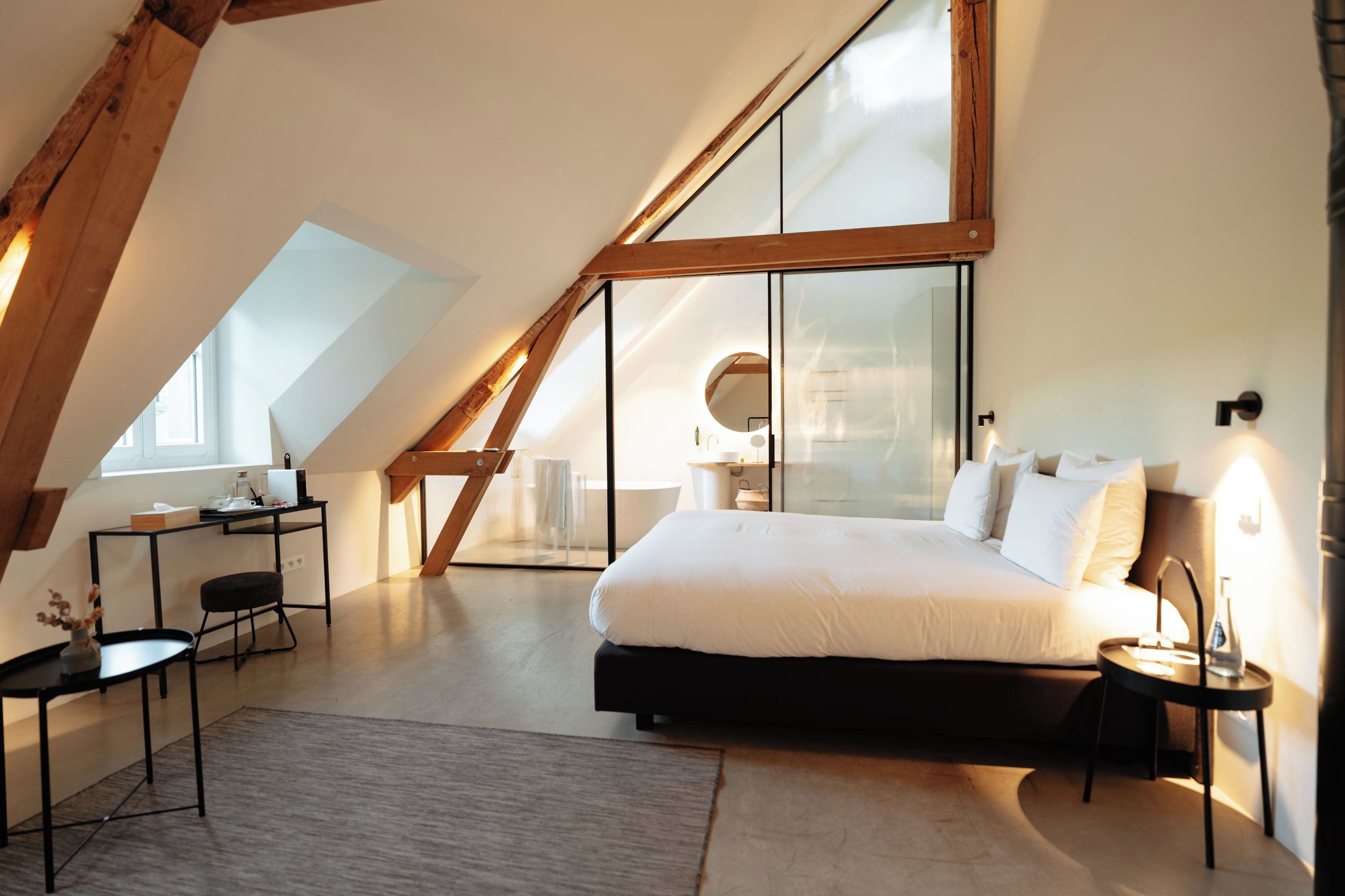 Un dormitorio moderno con techo inclinado, una cama grande, un escritorio y una silla.