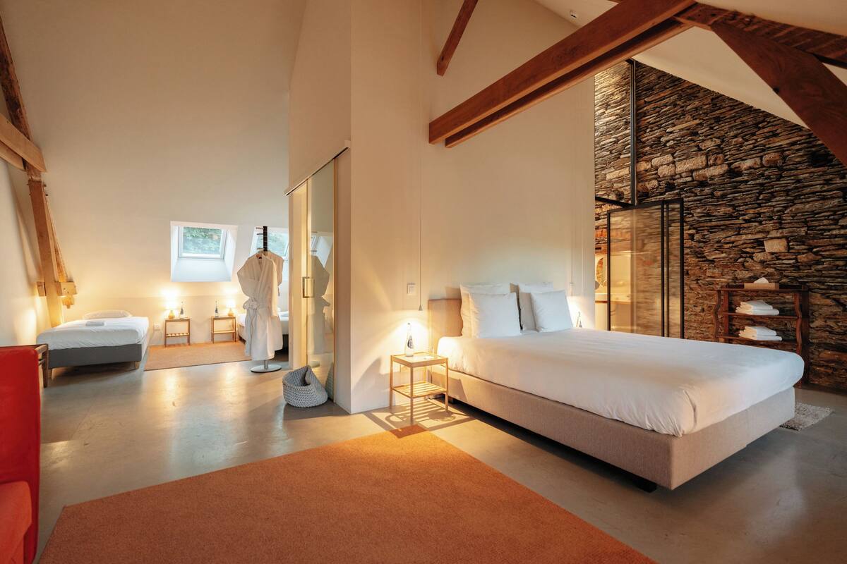 Ein Schlafzimmer mit einem großen Bett, einer Steinwand, einem Oberlicht und einem roten Sessel.