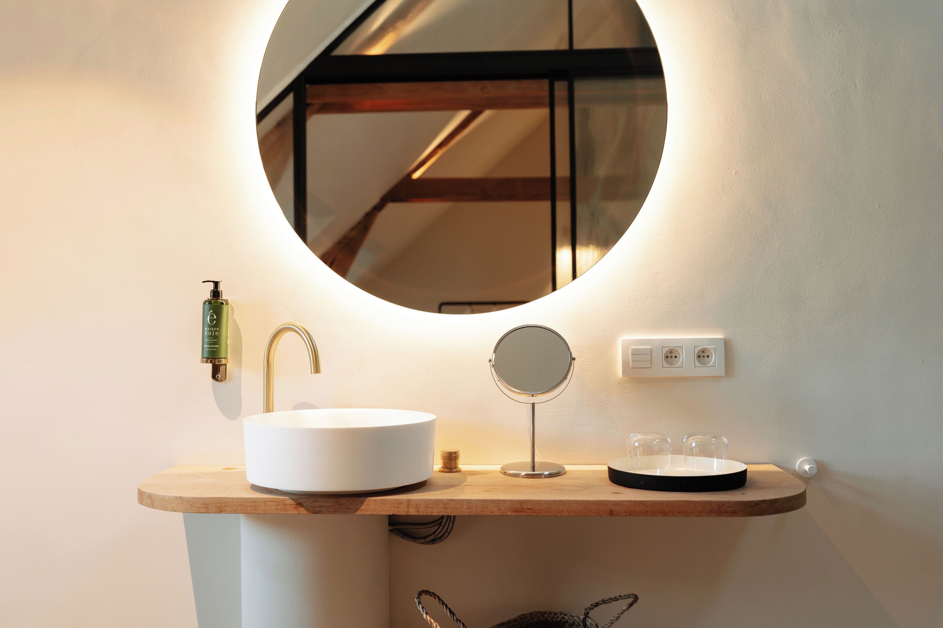 A bathroom with a round mirror, a white sink, and a soap dispenser.
