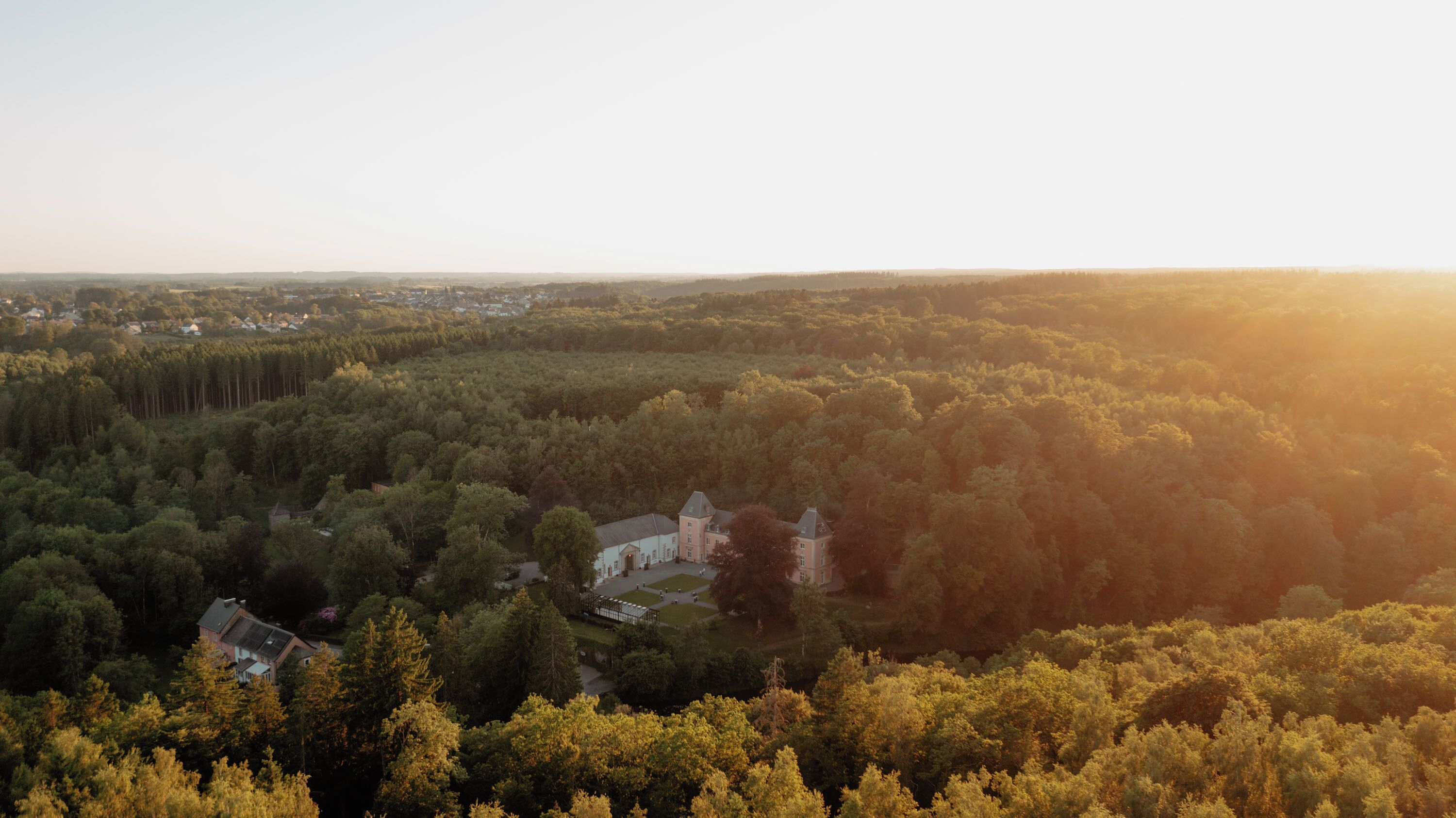 An aerial view of a forested area with a large estate featuring a main building and several smaller structures.