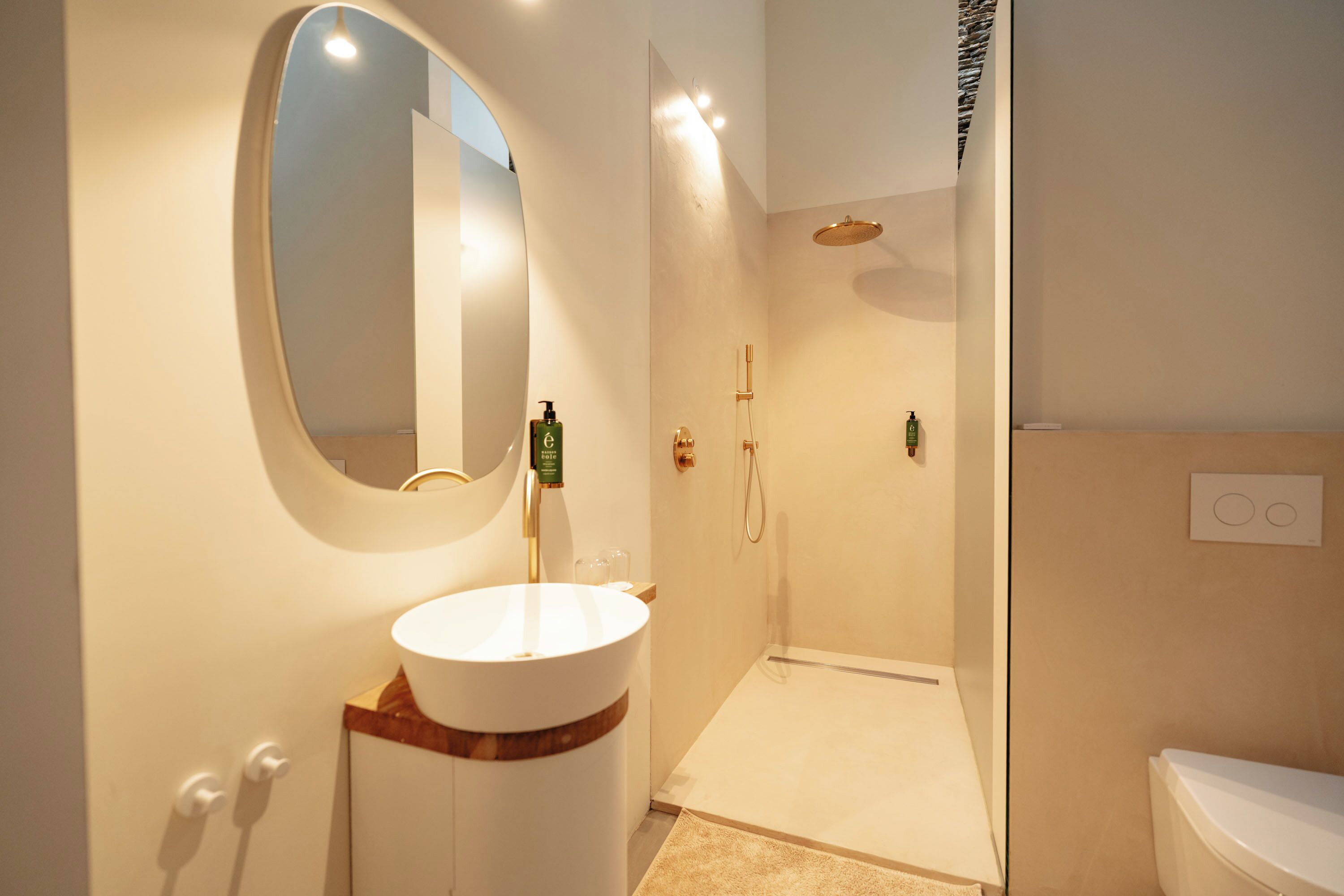 Un baño con un espejo redondo, un lavamanos blanco, una ducha y un inodoro.