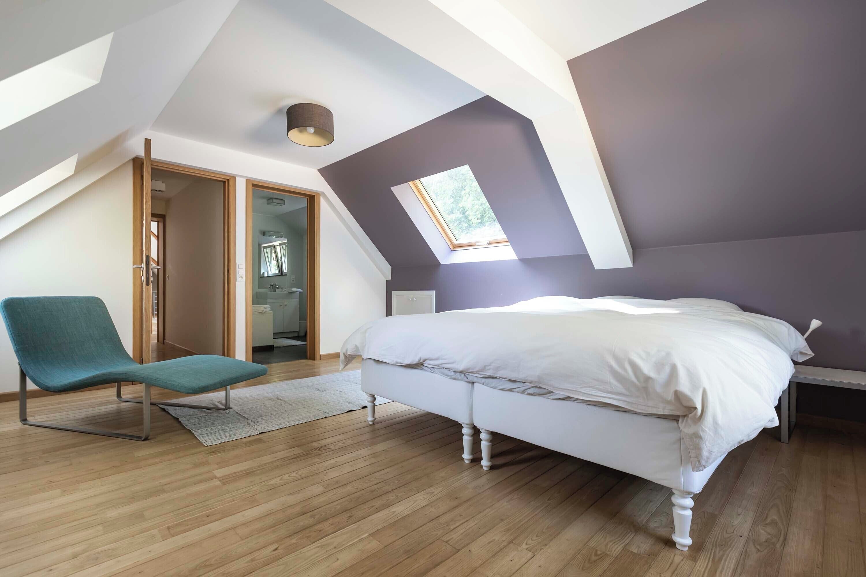 Quarto com teto inclinado, claraboia, cama, poltrona e closet espaçoso.