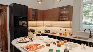 A modern kitchen with wooden cabinets, a built-in oven, and a breakfast bar with various food items and condiments. - Château du Pont d'Oye (Habay)