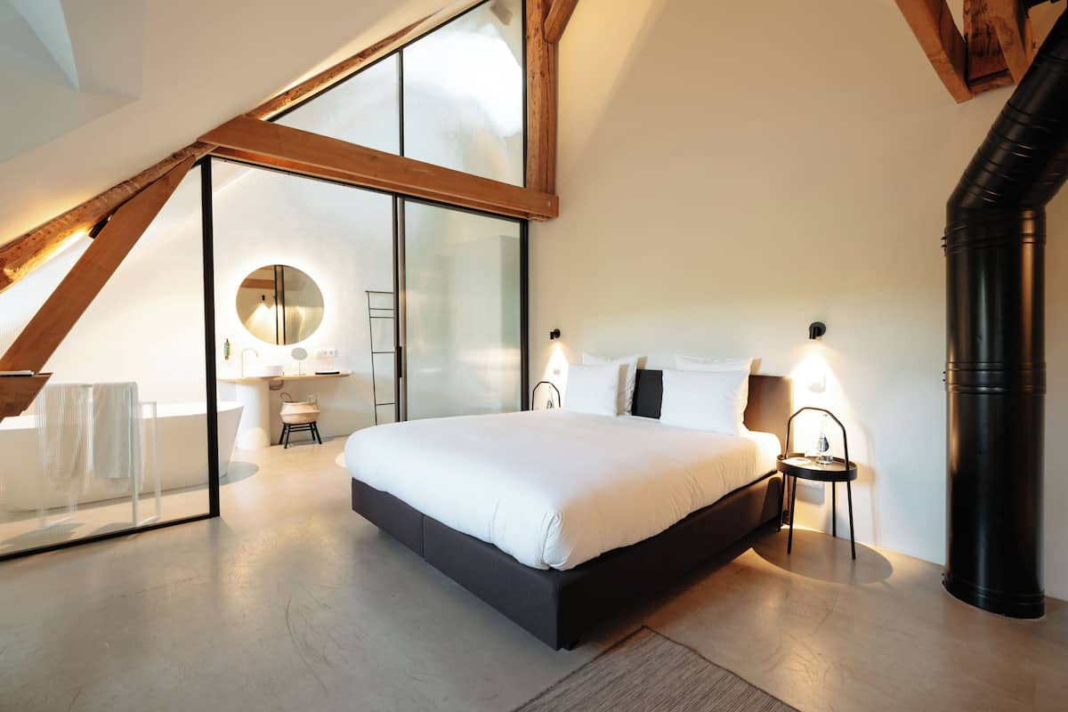 Ein Schlafzimmer mit einem großen Bett, einem Oberlicht, einer Holzbalkendecke und einer schwarzen Rohrleitung.
