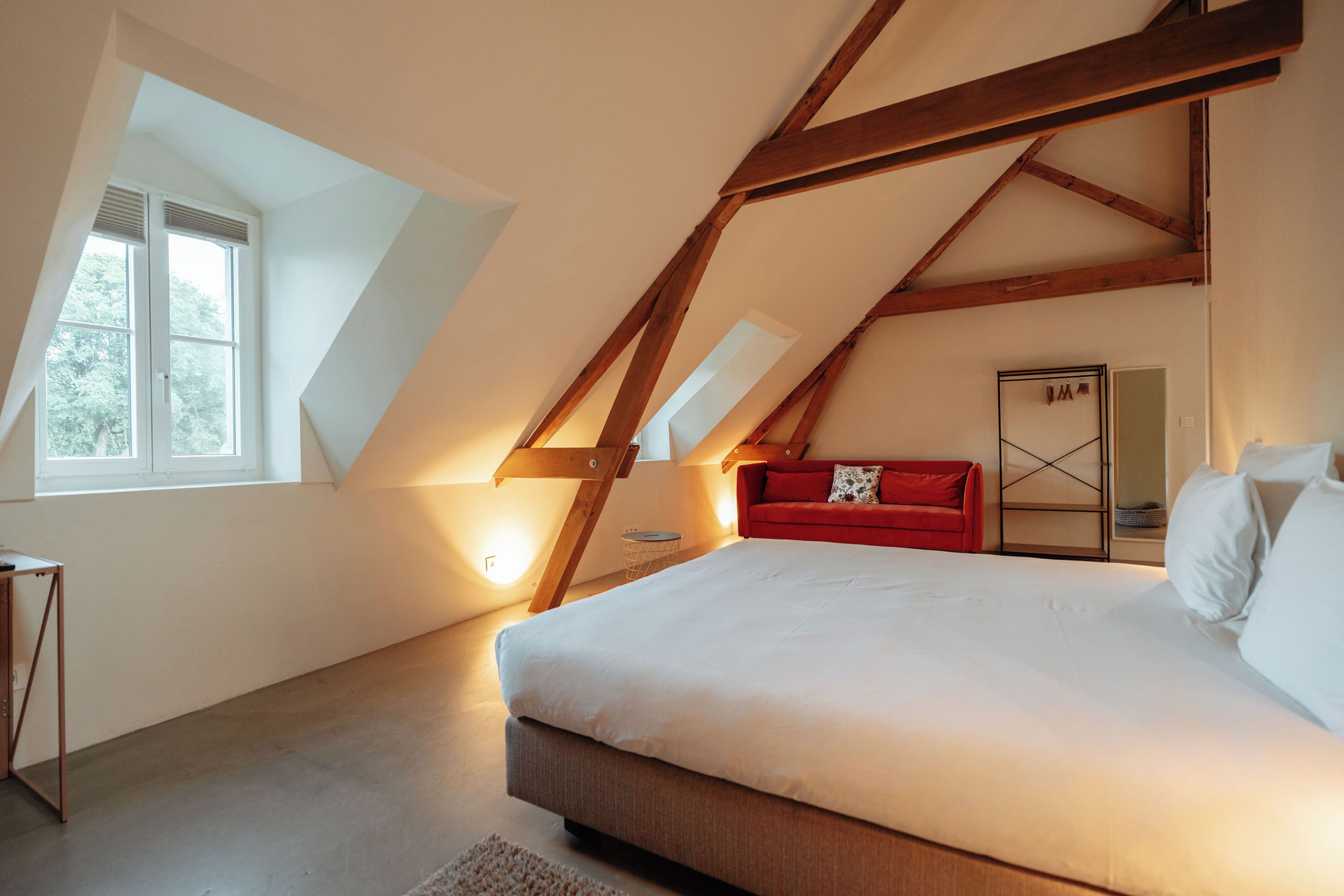 A bedroom with a large bed, a red sofa, and a skylight.