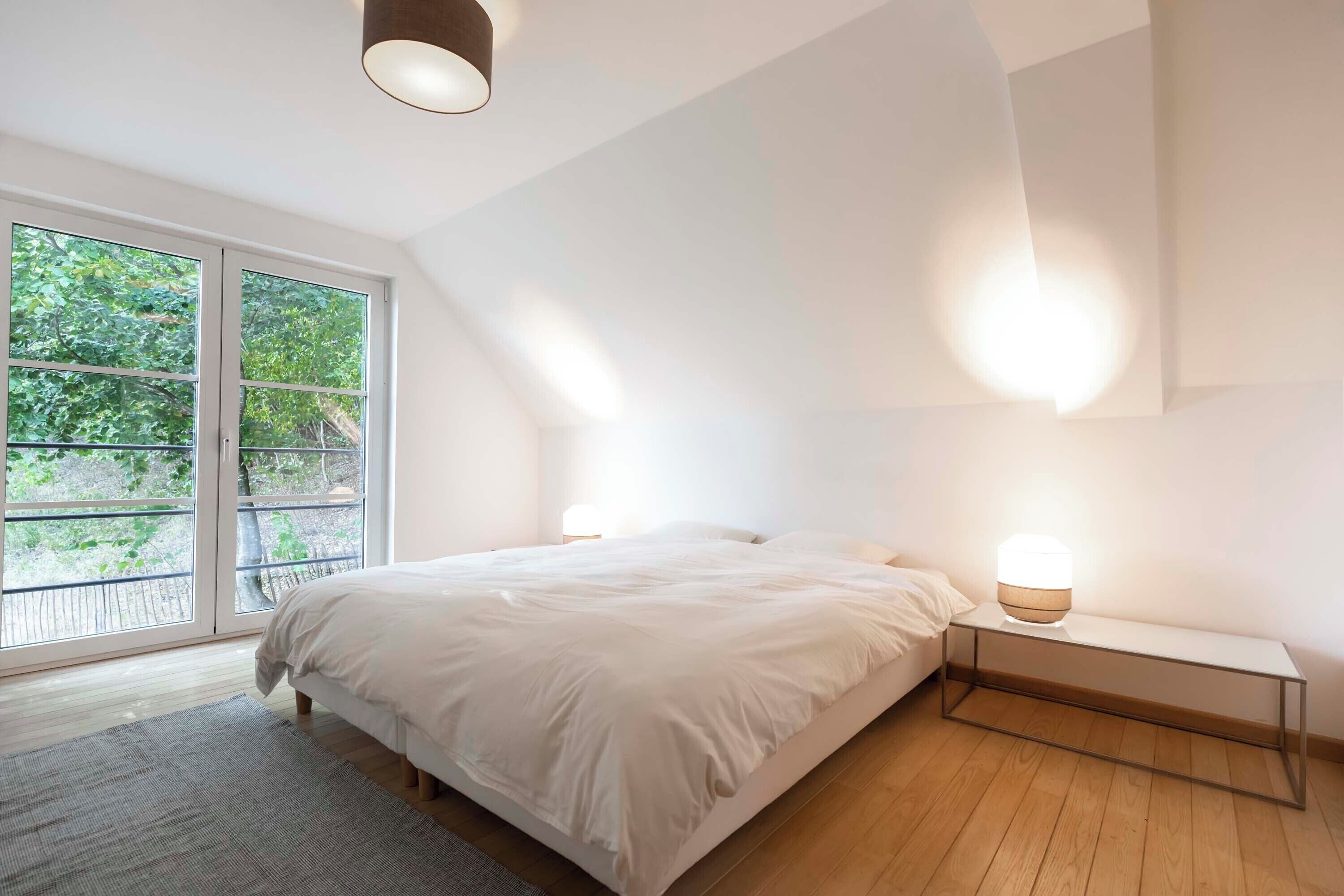 Un dormitorio con una ventana grande, una cama, mesitas de noche y una lámpara en el techo.