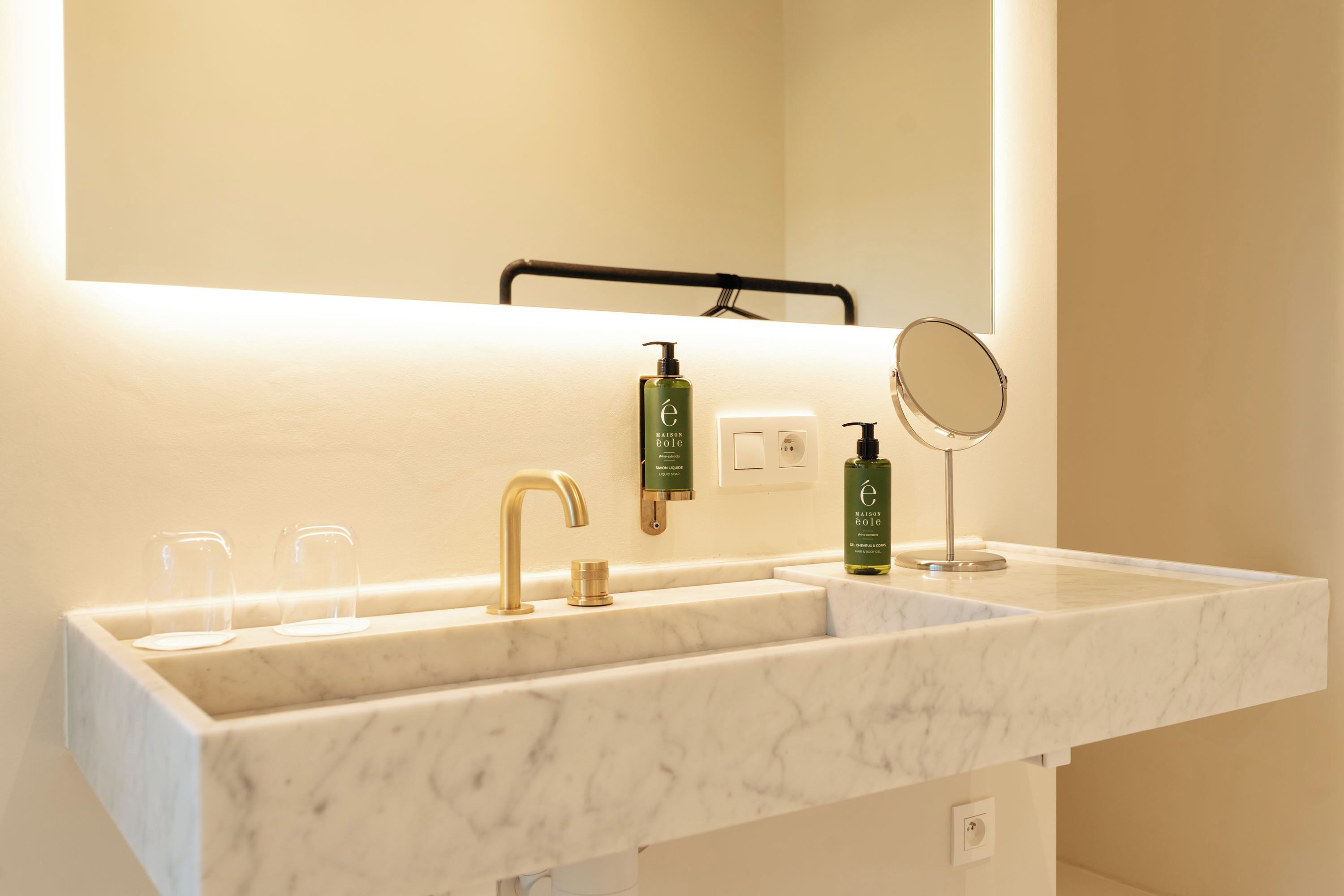 A bathroom with a marble sink, a gold faucet, a mirror, and two bottles of lotion.