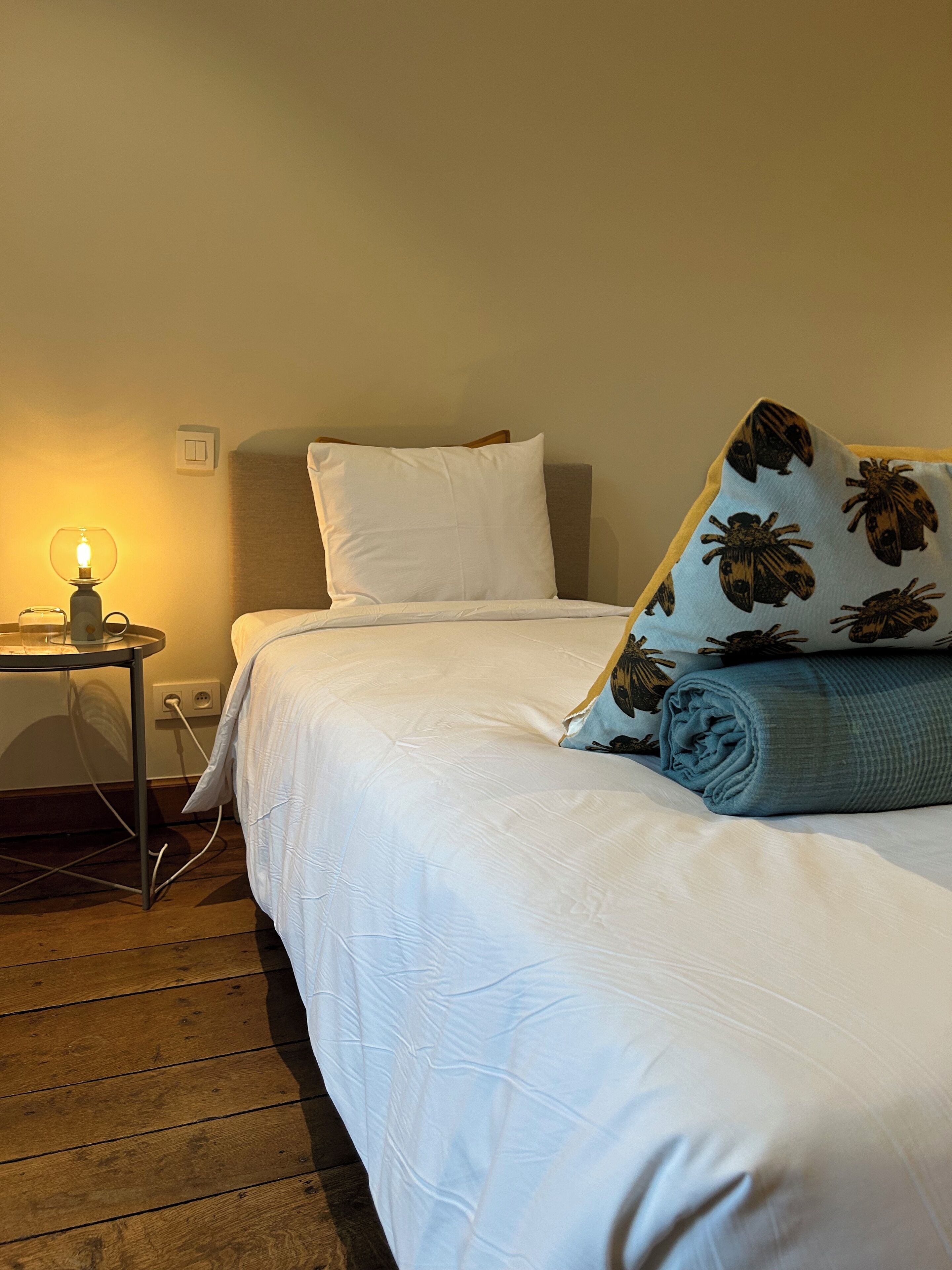 Una cama bien hecha con ropa de cama blanca y una almohada azul estampada con motivos florales.