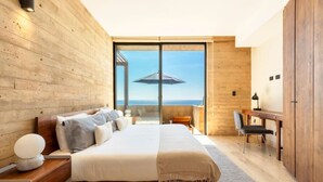 A modern bedroom with a large bed, a desk, and a view of the sea through large windows. - Panoramic Ocean View - Hot Tub (San José del Cabo)