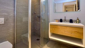 Un bany modern amb dutxa de vidre, un tocador de fusta i un mirall sobre el lavabo.