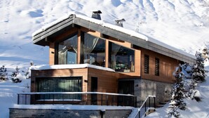 Una casa moderna de dos pisos amb grans finestres, un balcó i un sòcol de pedra, envoltada de neu.