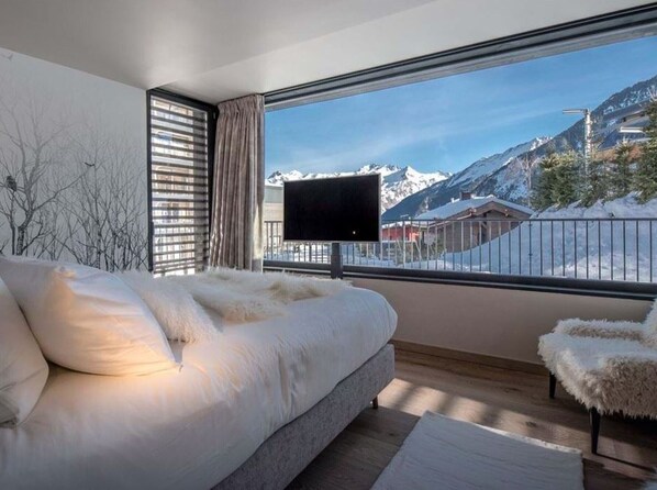 Een slaapkamer met een groot bed, een televisie op een balkon en uitzicht op een besneeuwde berg.