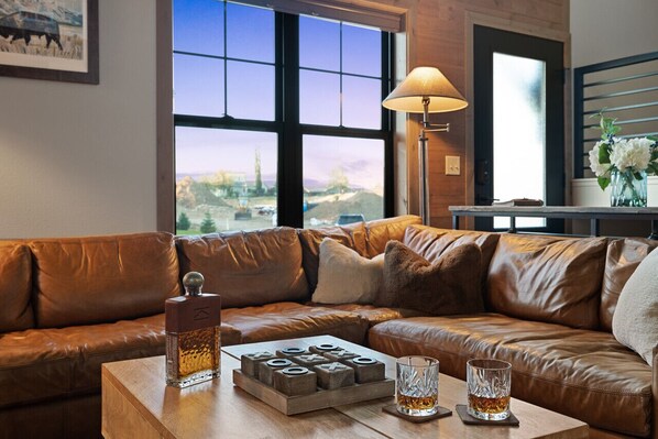 A modern living room with a leather sofa, a wooden coffee table with a bottle, glasses, and a board game. - Private hot tub, large home, close to downtown (Red Lodge)