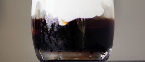 A glass of dark liquid with a white foam on top, placed on a textured surface.