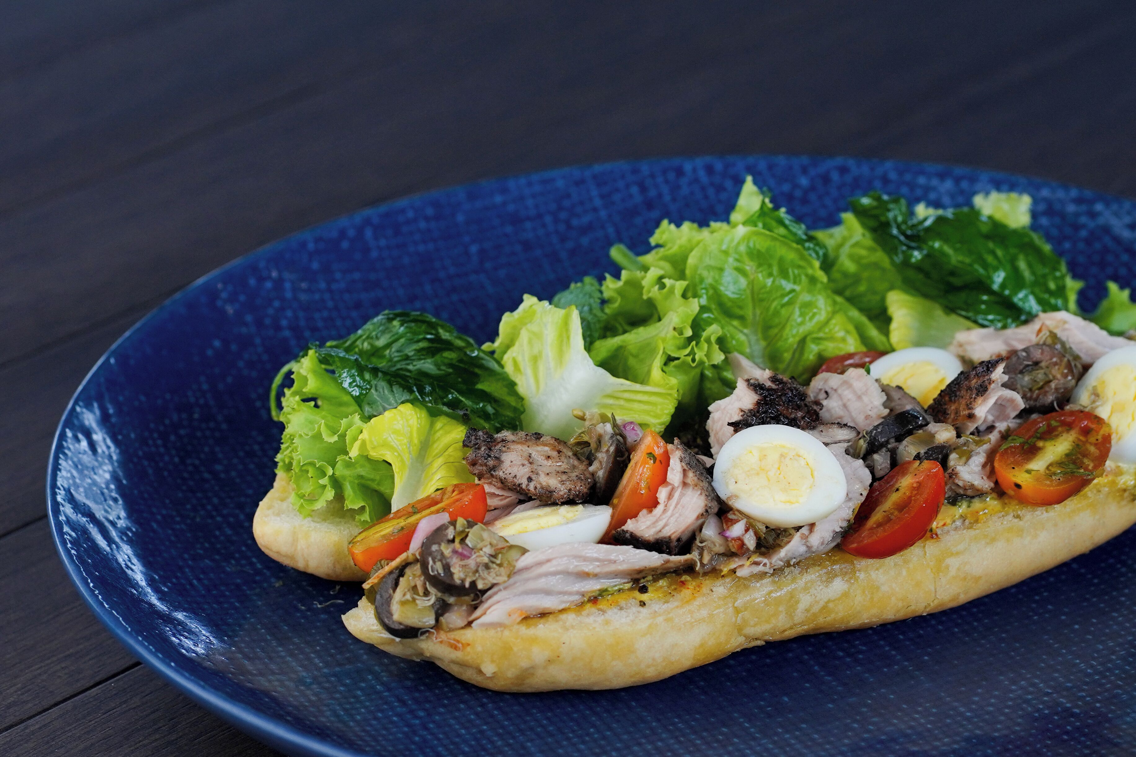 A sandwich with meat, eggs, and vegetables on a blue plate.