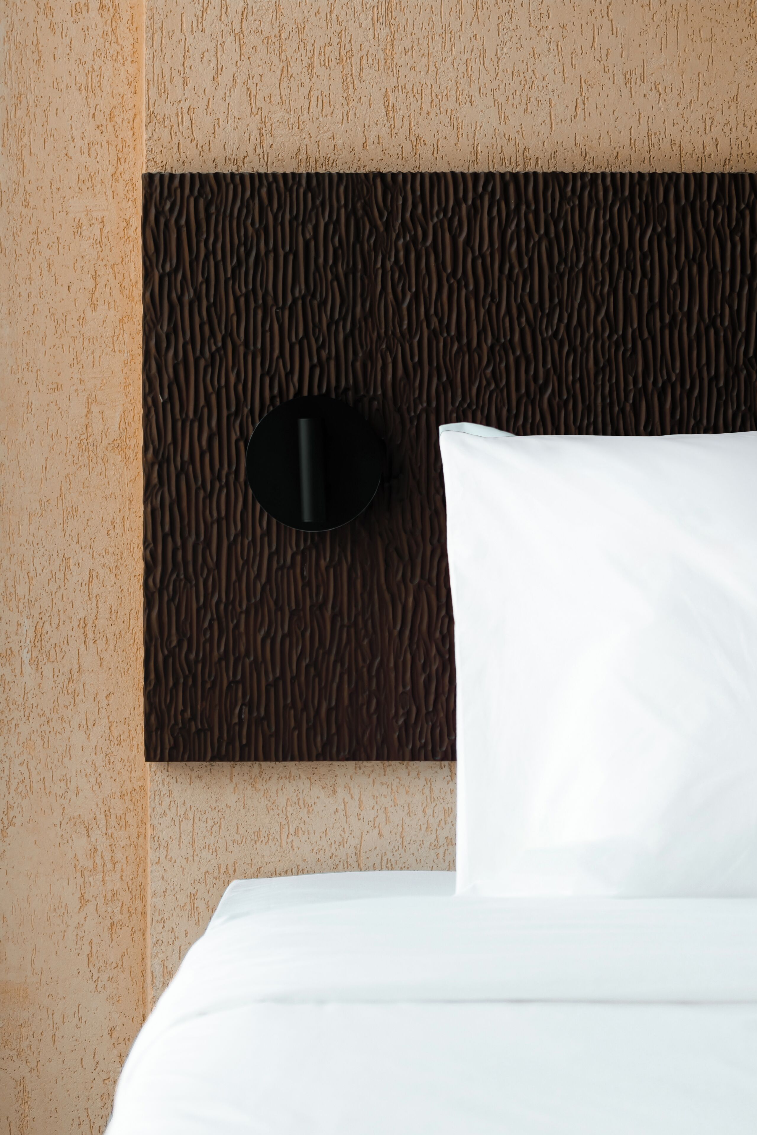 Una cama con ropa de cama blanca y un cabecero con textura.