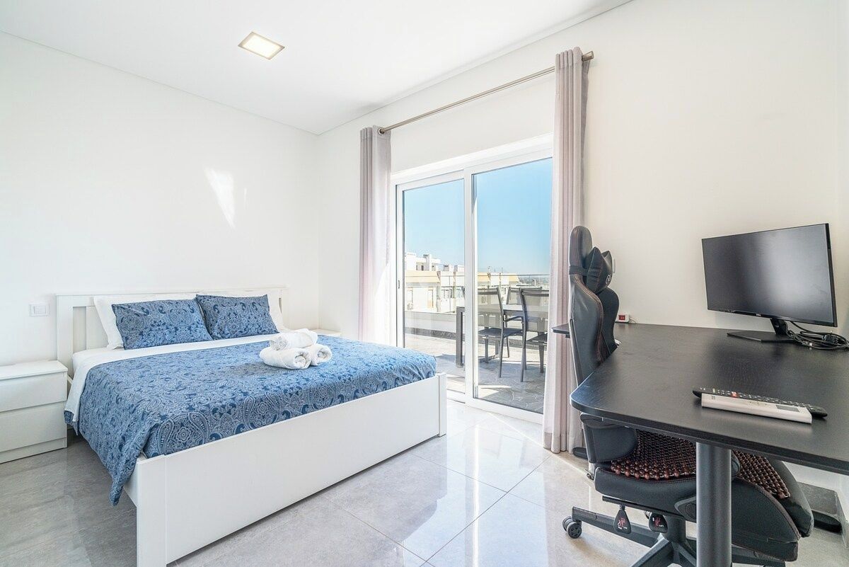 A hotel room with a bed, a desk with a computer, a TV, and a view of the outside.