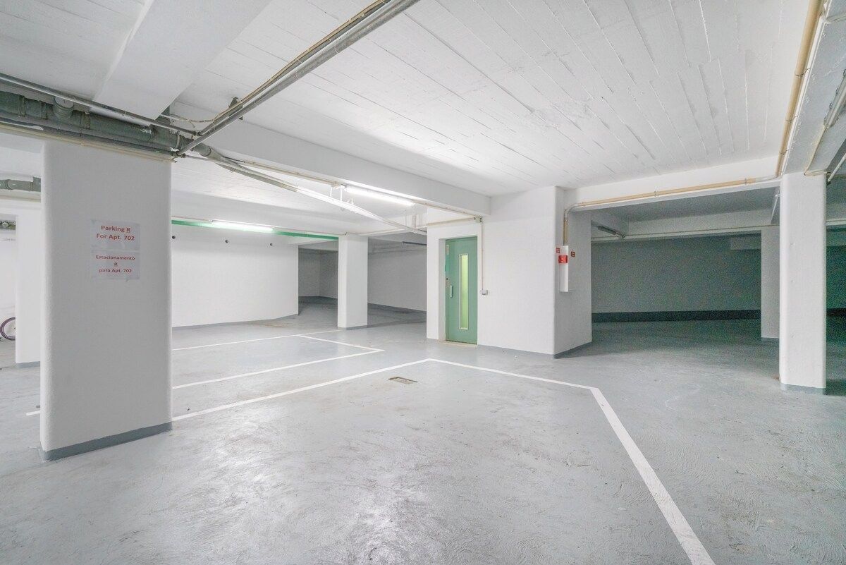 A parking garage with white walls and concrete floors, marked parking spaces, and a green exit door.