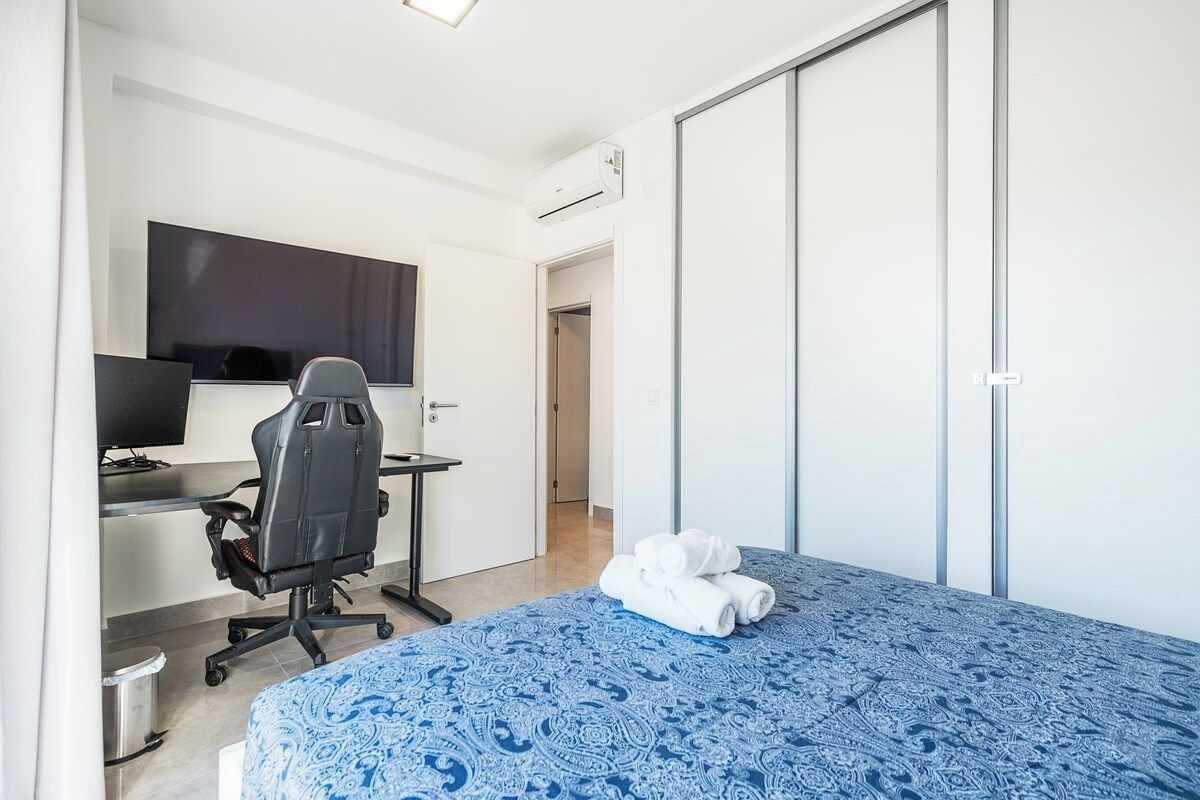 A bedroom with a bed, a desk with a computer, a chair, and a television.