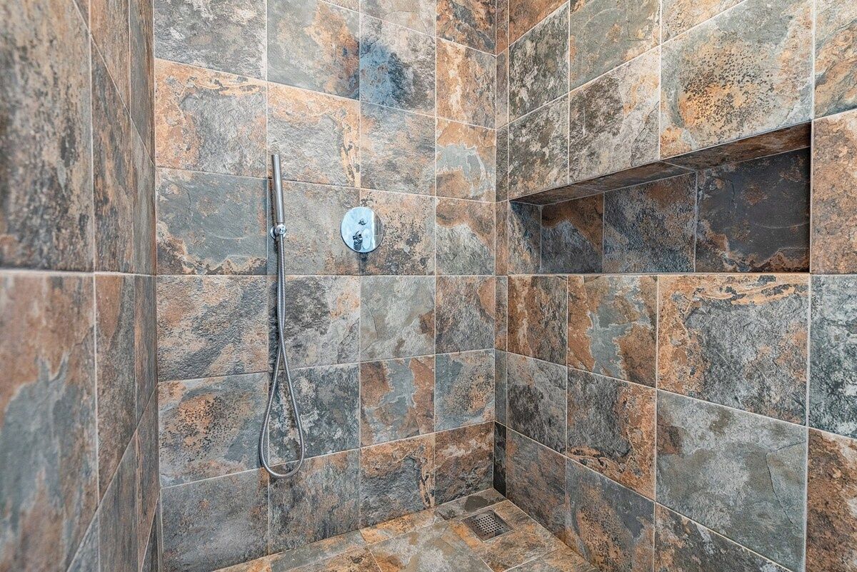 A shower area with a handheld showerhead and a control panel on the wall.