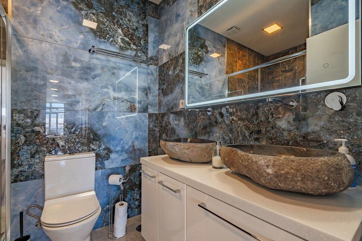 A bathroom with a marble backsplash, a large mirror, a toilet, and a stone basin sink.