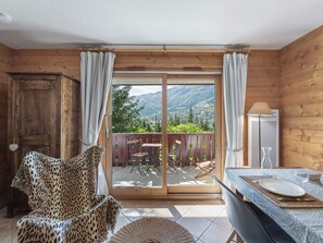 Eine Holzhütte mit Essbereich, einem Sessel mit Leopardenmuster und Blick auf Berge durch eine Schiebetür.