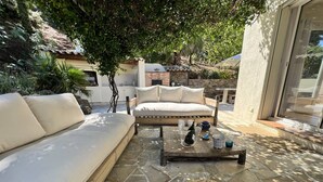An outdoor seating area with a sofa and a coffee table, surrounded by stone flooring and greenery. - Luxurious Villa: 4 Bedrooms, Heated Pool, Stylish Interiors, Near Village in La Croix-Valmer (La Croix-Valmer)