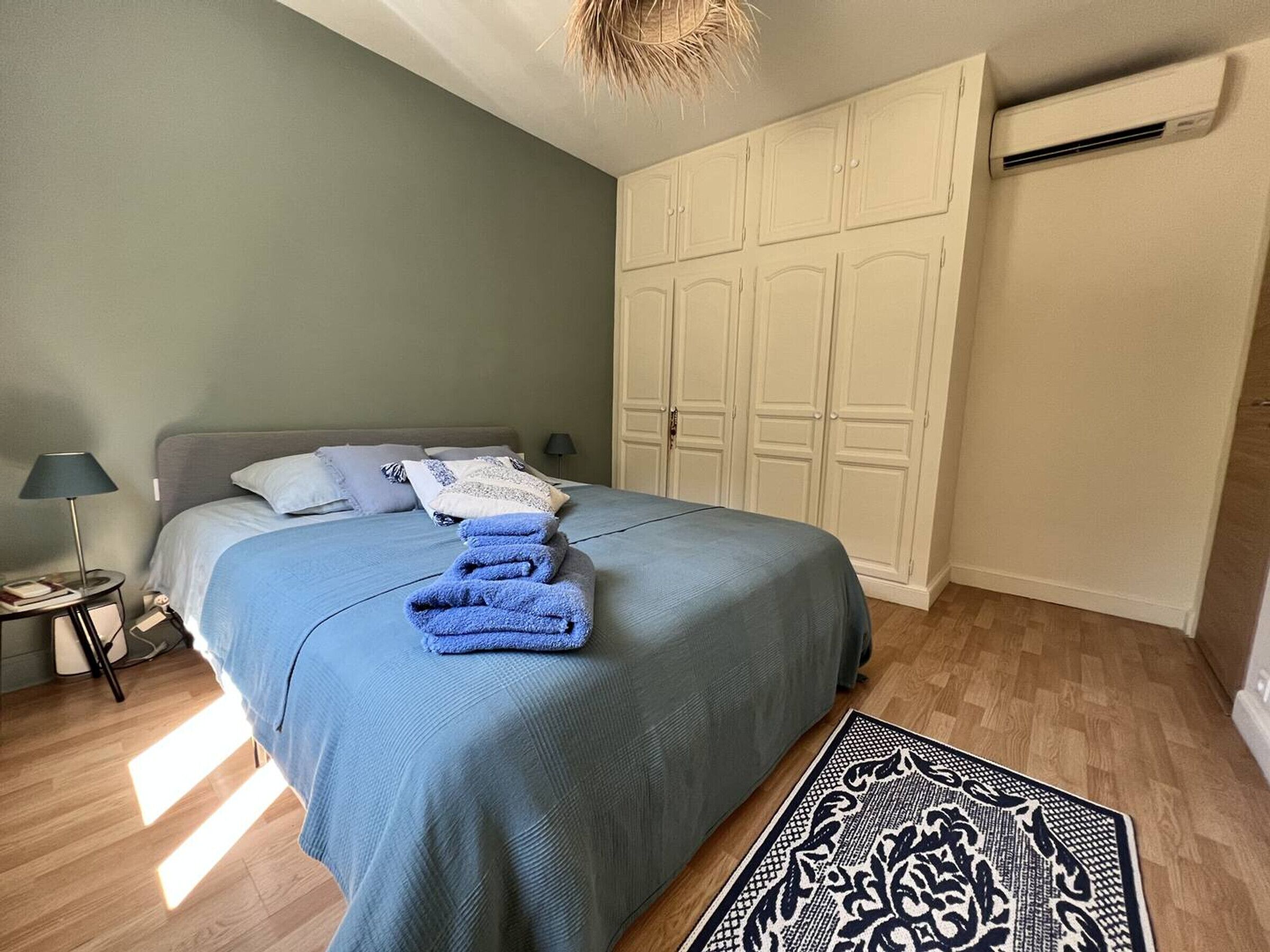 Une chambre à coucher comprenant un lit, une table de chevet, une lampe, une armoire et un tapis à motifs.
