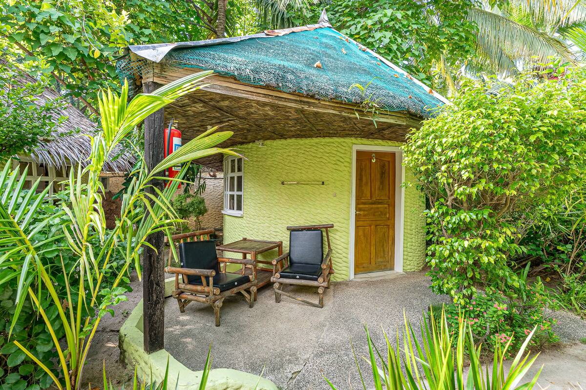 A small, green-roofed hut with a wooden door, two wooden chairs, and a table.