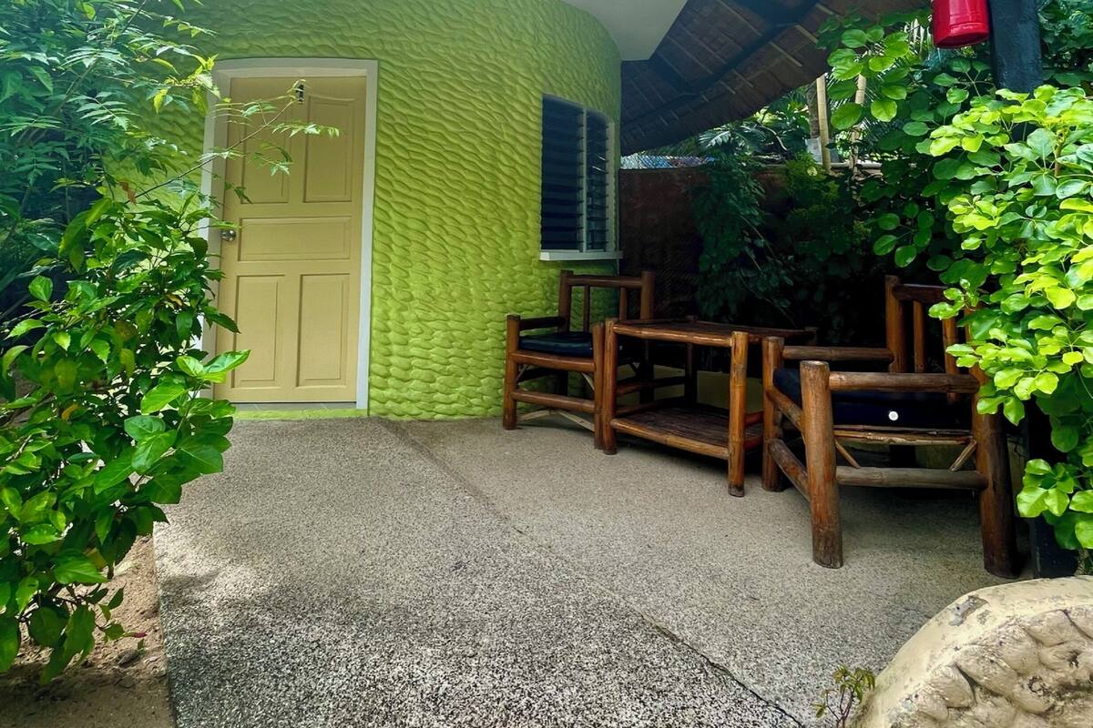 A building with a green textured wall, a wooden door, and a covered porch area with wooden furniture.